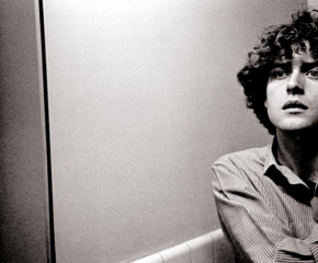 Black and white photograph of a man seen from mid torso up, wearing a button-down shirt and looking up