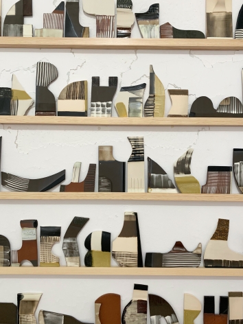 a detail of Katy Fischer's site-specific installation featuring several ceramic tiles of various shapes on wood shelves vertically stacked on one another.