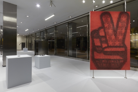 Various works of art by Adam McEwen presented at the Lever House Art Collection. The walls are ceiling to floor glass windows which show that it is night time.