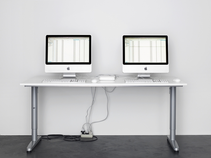 Two Apple iMac computers, side by side, displaying data on a white table, mounted on an ikea table.