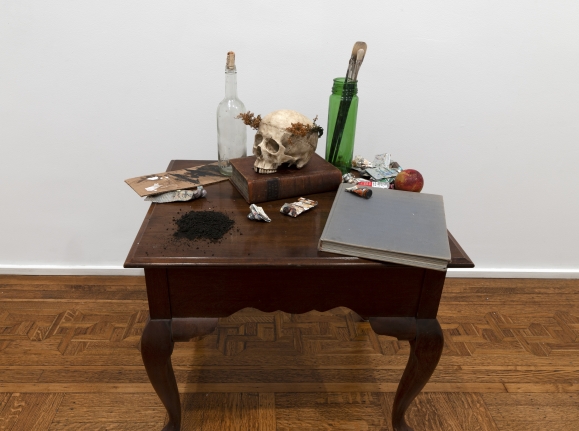 Merik Goma Memento Mori, 2019 Table, books, paints, plastic skull, flower crown, glass Installed dimensions variable