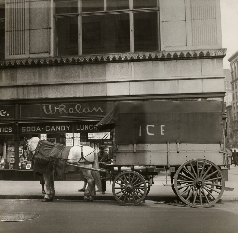 Cecil Beaton, New York, c. 1935. A horse-drawn carriage marked "Ice" on the street in front of a building marked "Whelan Soda Candy Lunch"