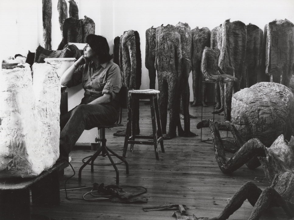 Black and white photographic portrait of Magdalena Abakanowicz in her studio surrounded by sculptures