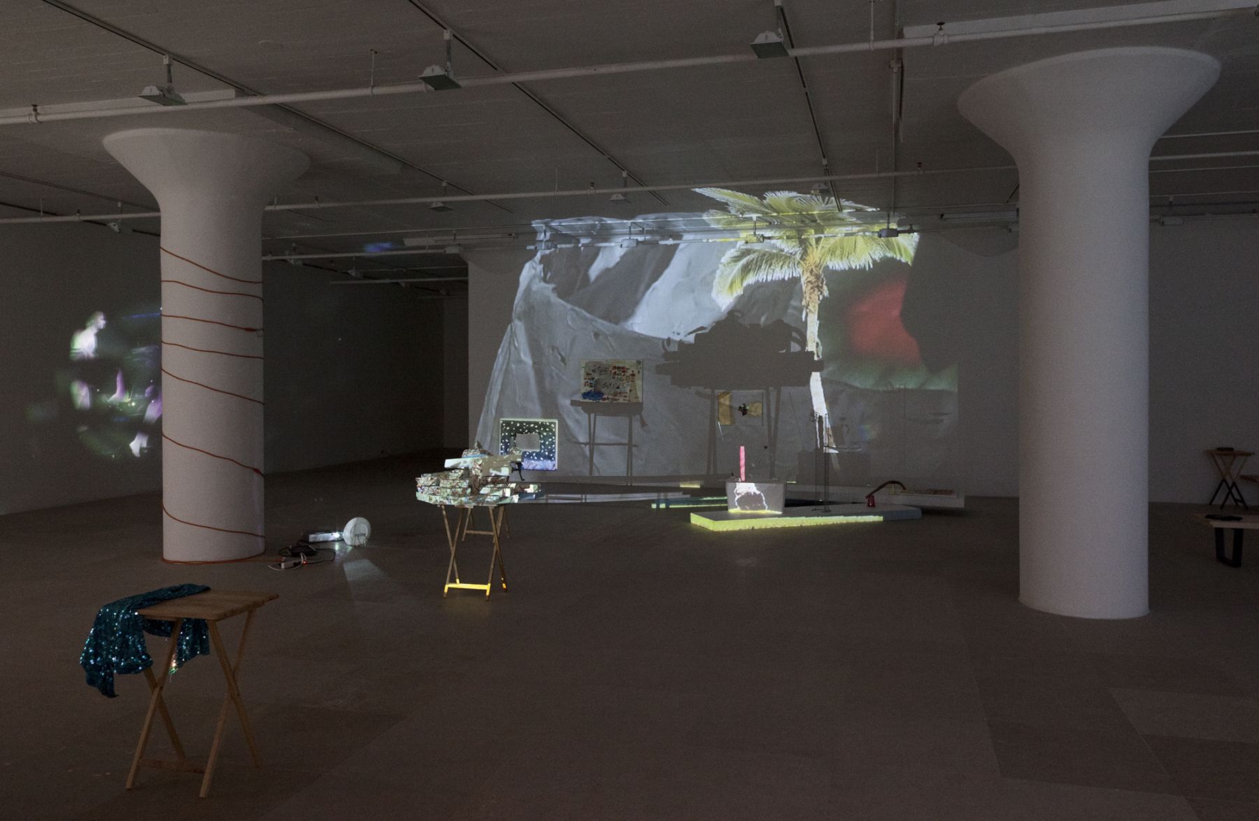 Bag's Circle, 2012, Single-channel video installation with four acrylic-on-canvas paintings, painted foam sculptures, CD rack, plastic cups, sticks, plexiglass, tape, clay, three folding tables, sequined throw, extendable fork, Continuous loop, Dimensions variable