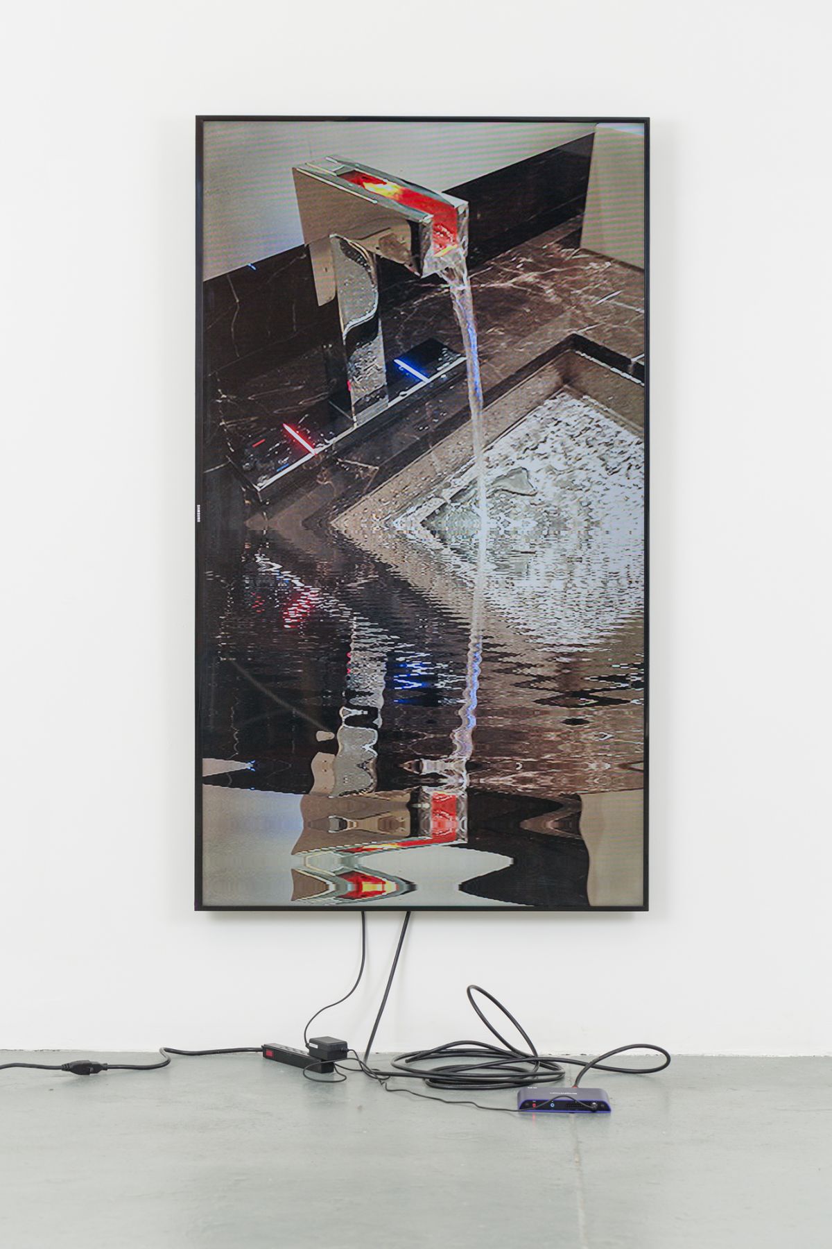 A vertically aligned television monitor displaying a running sink mounted on a granite countertop. The water reflects the image of the sink, distorted.