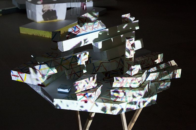 Bag's Circle, 2012, Single-channel video installation with four acrylic-on-canvas paintings, painted foam sculptures, CD rack, plastic cups, sticks, plexiglass, tape, clay, three folding tables, sequined throw, extendable fork, Continuous loop, Dimensions variable