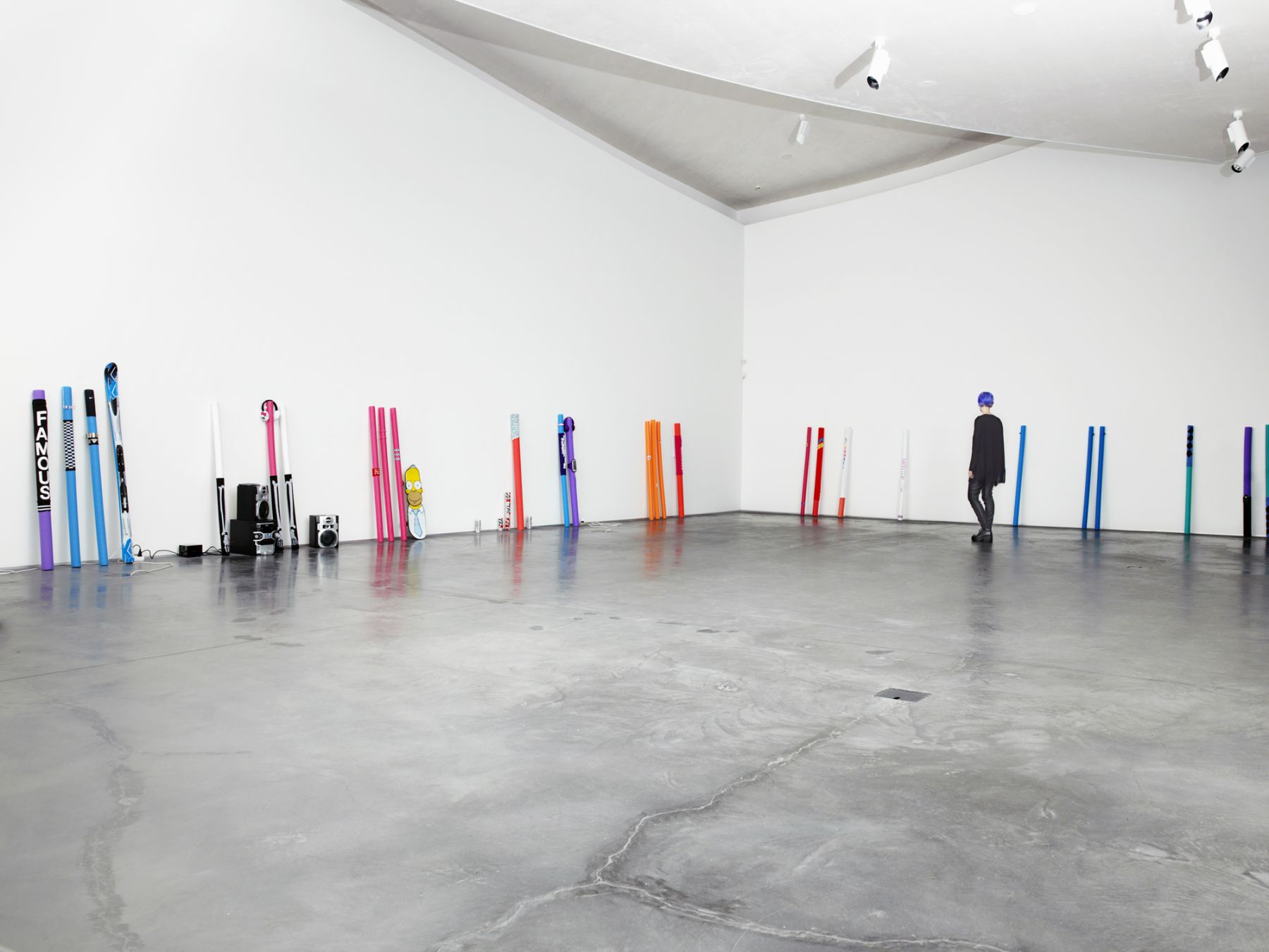 Multicolored skiis, hockey sticks, headphones, and a stereo set aligned upright along the bottom of two walls.