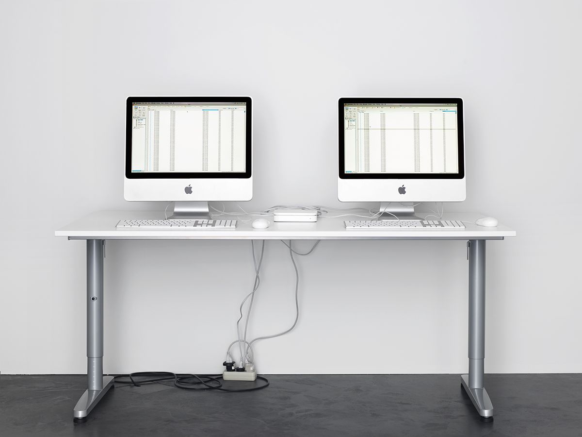 Two Apple iMac computers, side by side, displaying data on a white table, mounted on an ikea table.