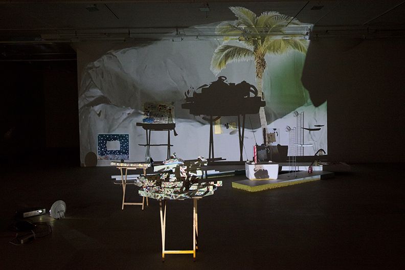 Bag's Circle, 2012, Single-channel video installation with four acrylic-on-canvas paintings, painted foam sculptures, CD rack, plastic cups, sticks, plexiglass, tape, clay, three folding tables, sequined throw, extendable fork, Continuous loop, Dimensions variable