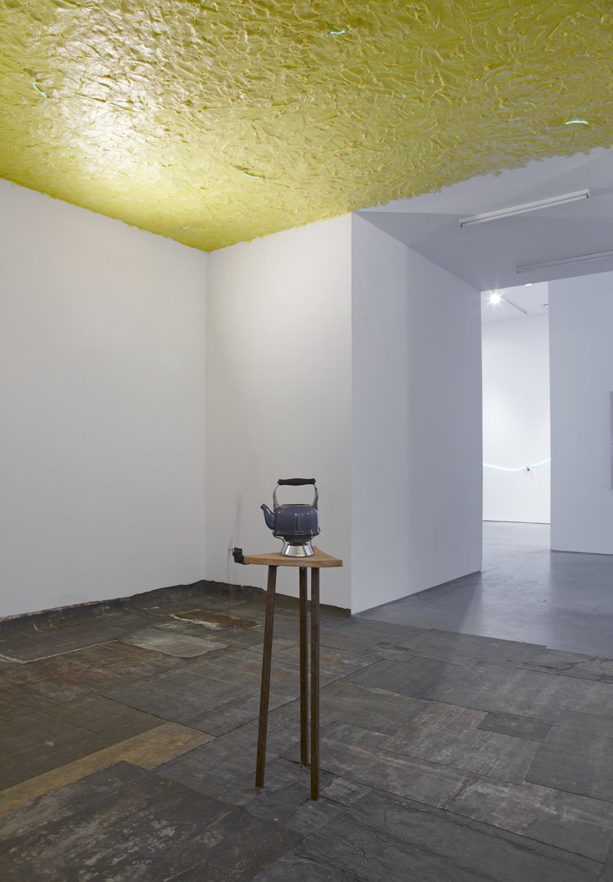 installation by pier paolo calzolari featuring a teapot on a wooden pedestal and a yellow, waxy ceiling