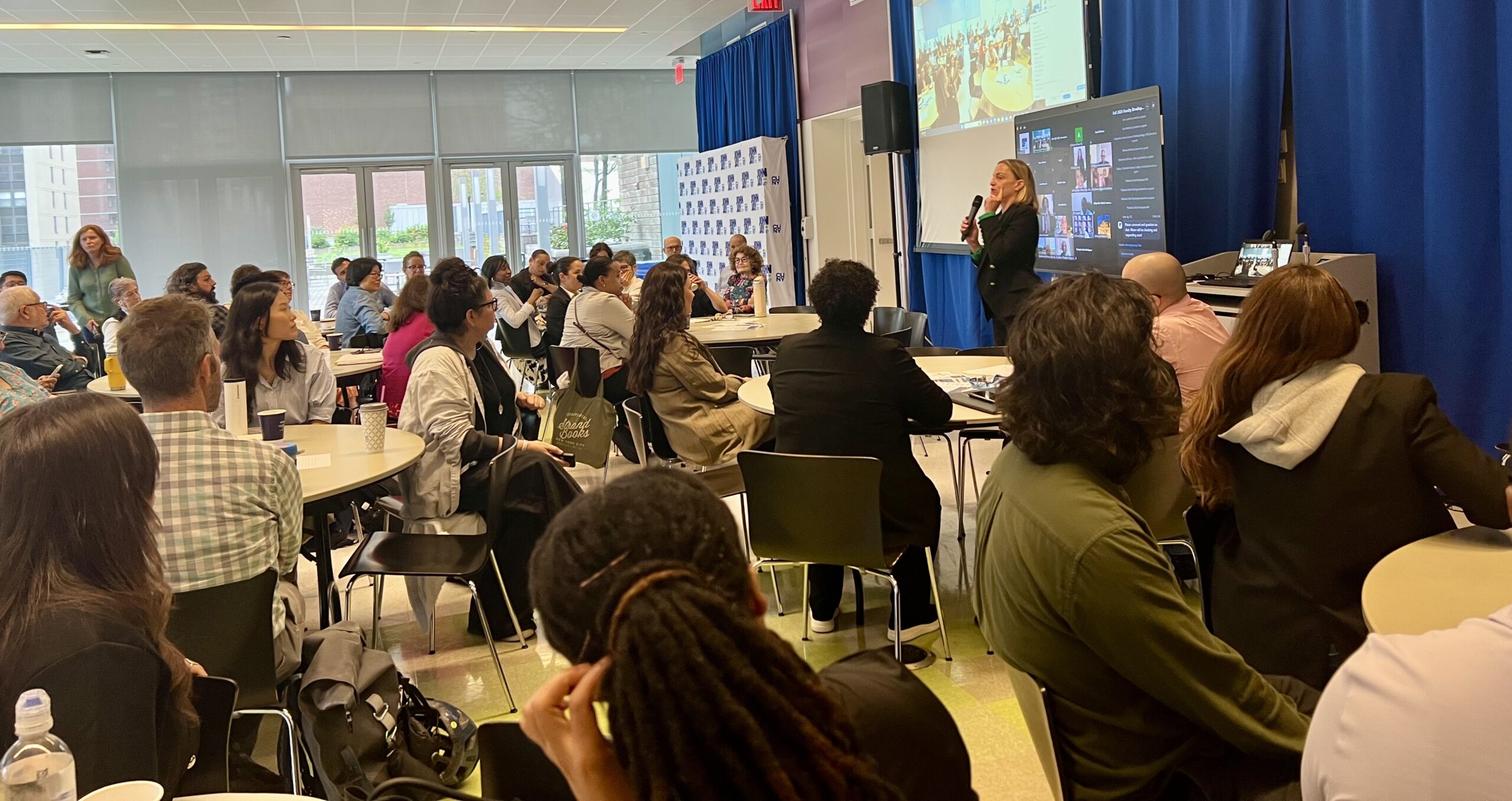 Provost Allison Pease standing and speaking to a full room of faculty seated at round tables in a large space.