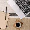 bird's eye view of a table with a laptop, notepad, pencil, and coffee