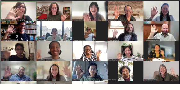 A large group of people smiling and waving on zoom