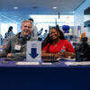 People smiling behind a career fair table.