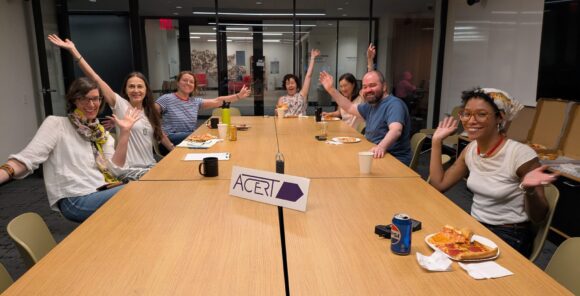 People sitting at a table, smile and pose for the camera with an "ACERT" sign in the middle of the table.