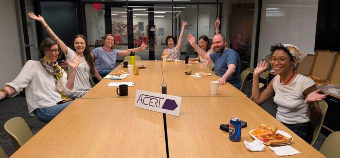 People sitting at a table, smile and pose for the camera with an "ACERT" sign in the middle of the table.