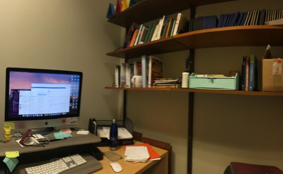 office with desk, computer, and bookshelves. lighting is dim and there are no windows