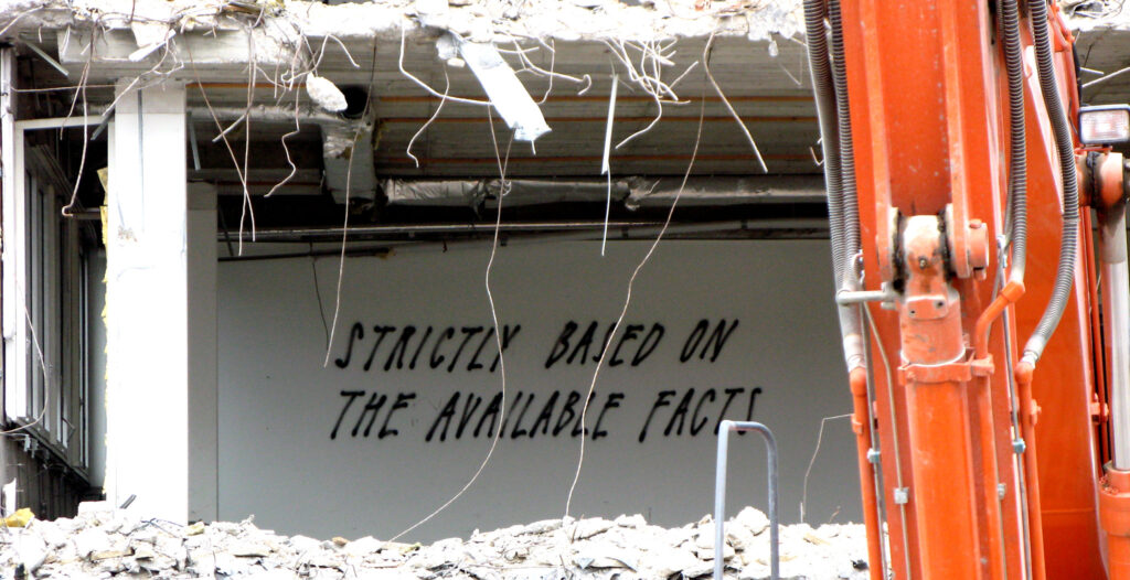 Spray painted words on a wall in a construction site reading "strictly based on the available facts."