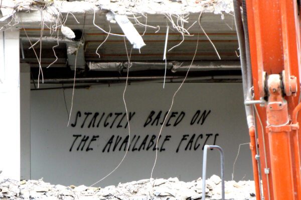 Spray painted words on a wall in a construction site reading "strictly based on the available facts."