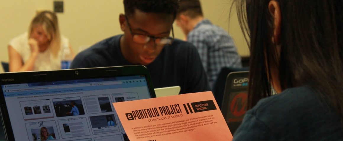 The image features a person, viewed from behind on the right side, reading a paper titled "ePortfolio Project: Reflective Writing." Behind the paper, a laptop is open. Several other students work in the background.
