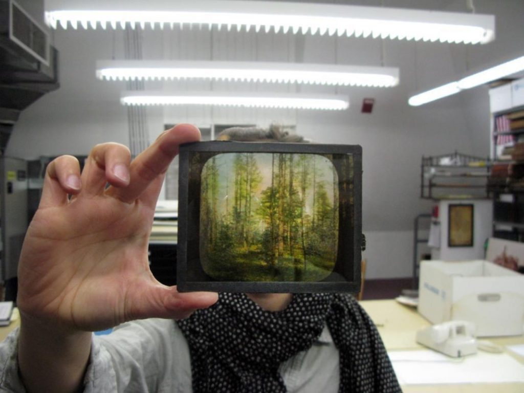 An image of a person whose face is hidden because they are holding up a colored lantern slide to the light