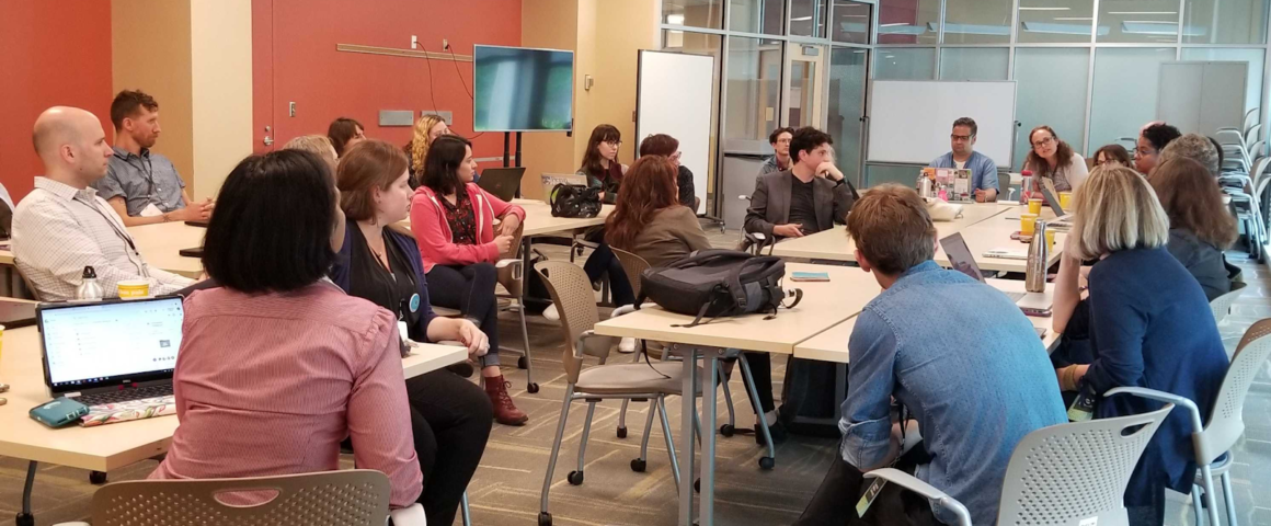 Group of twenty-one symposium attendees sitting in a circle actively engaged in a workshop discussion session.
