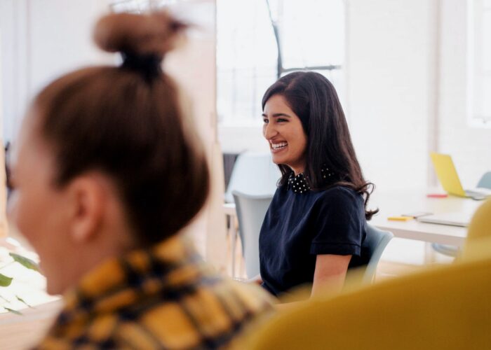 Two women smile laugh in an office setting.