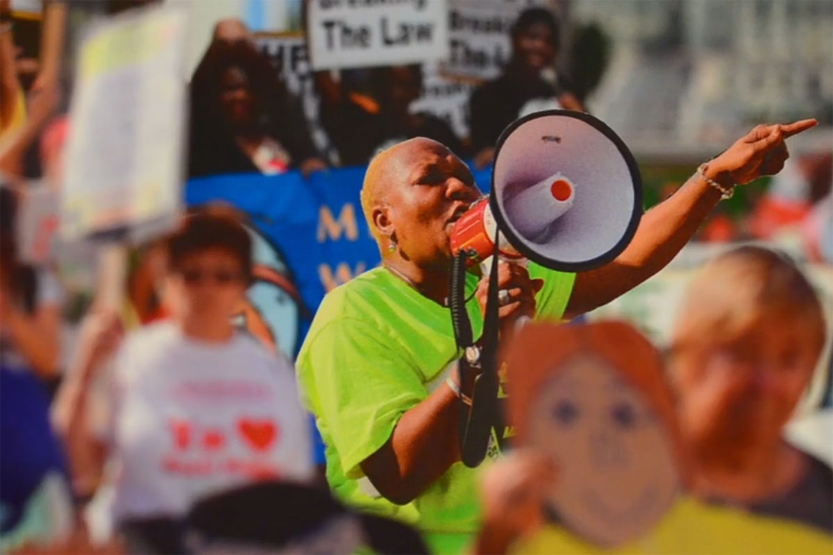 a woman shouting over a megaphone in a crowd of protesters
