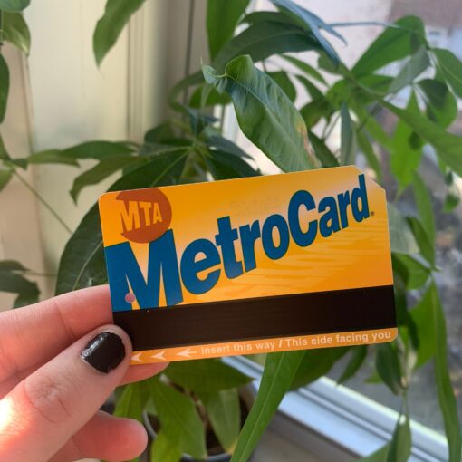image of a hand with naipolish hoding a MTA metro card with plant in the background