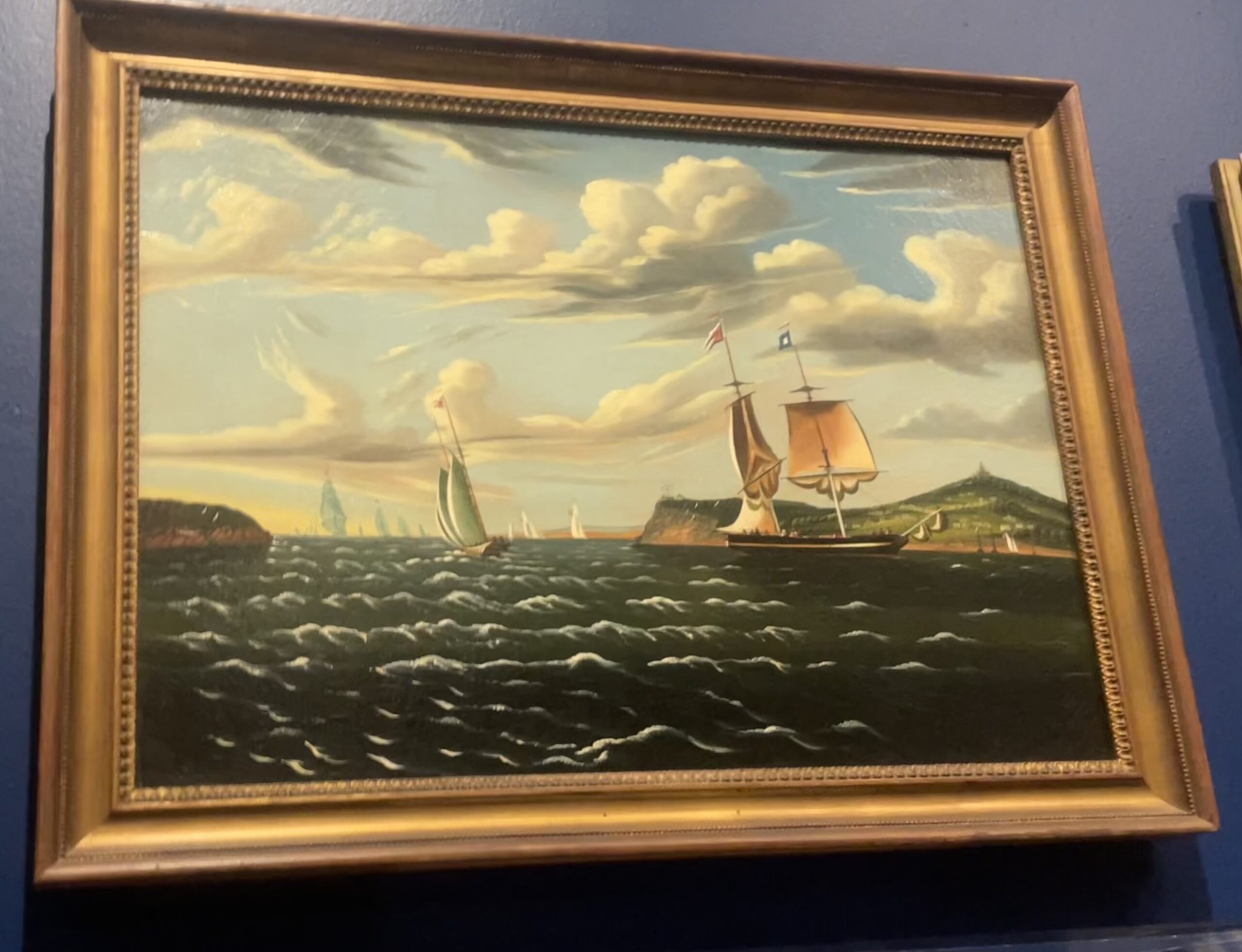 The painting is made of oil on a canvas, showing a landscape of Staten Island during the 1800s. The picture depicts a bloody of water with boats traveling through it in during dusk. There are 2 islands/lands visible where buildings are located.