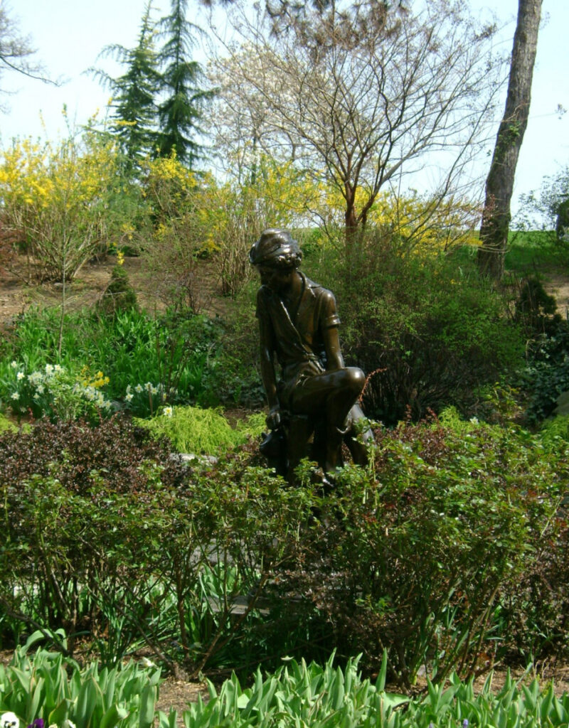 Bronze seated Peter Pan looking down among greenery
