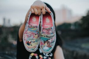 Unseen person holding a pair of slip on Disney Alice in Wonderland Van shoes