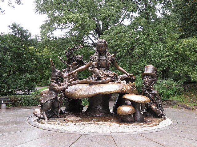 bronze statue of alice on toadstool with rabbit cat and hatter