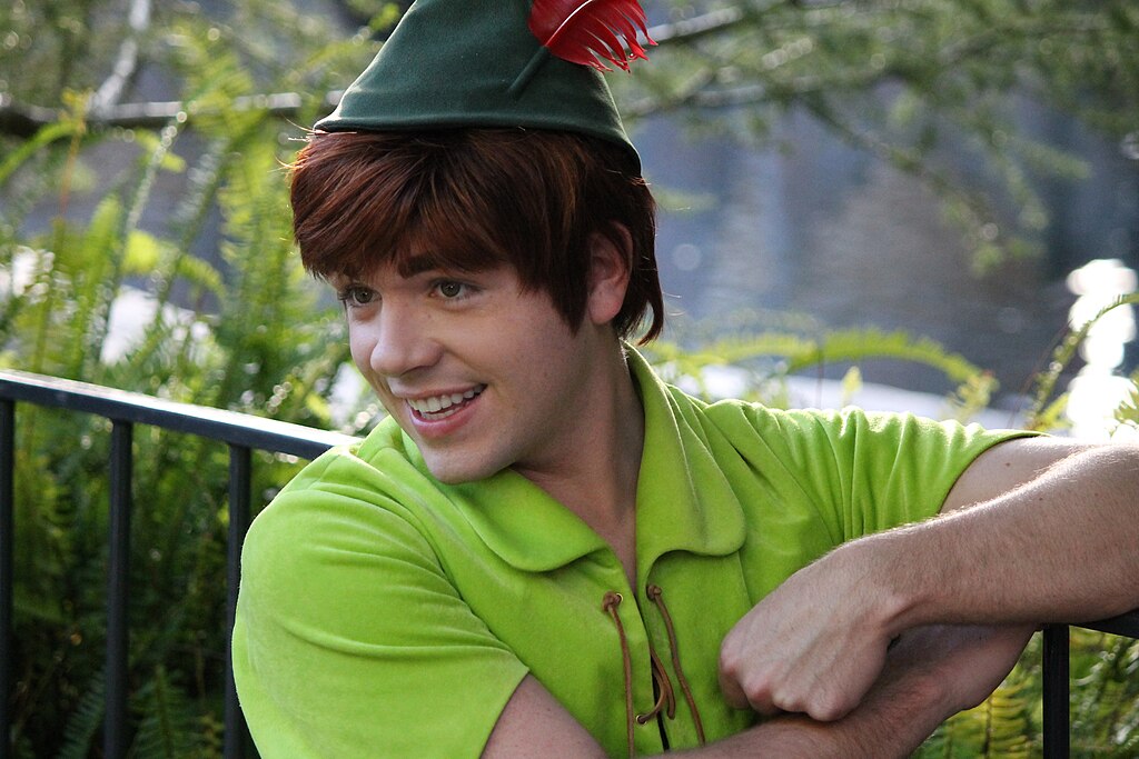 Photo of a man dressed as Disney's Peter Pan in a green top that ties, brown hair and a green hat with red feather leaning against a railing