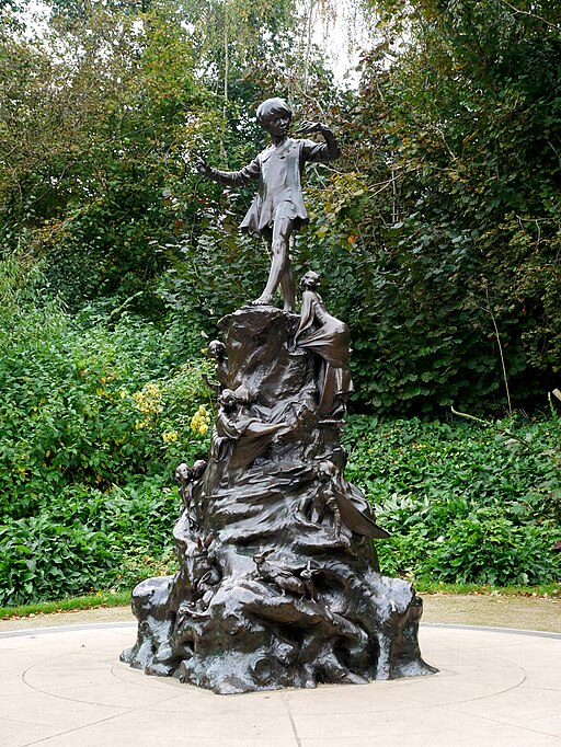Statue of a boy playing a small pipe on top of a sculpted block with fairies and other creatures.