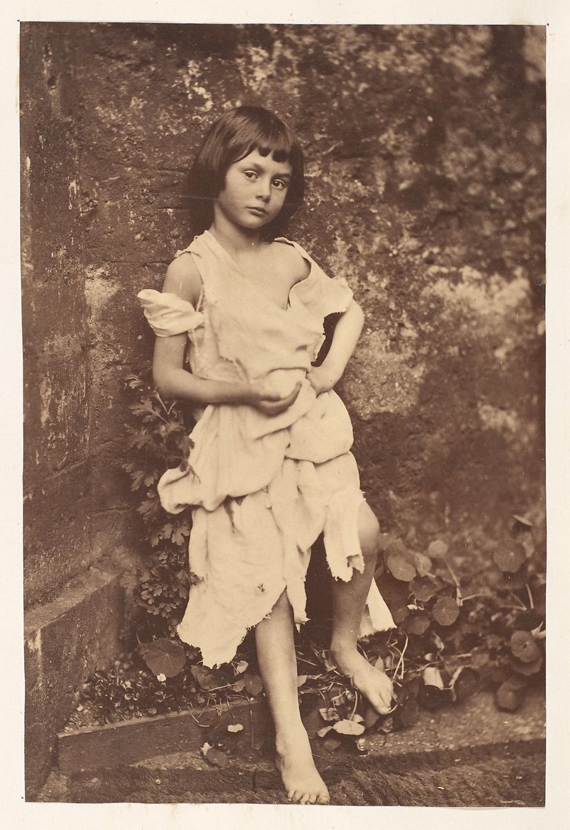 Sepia toned photograph of a young girl dressed in white rags, her shoulders are exposed and she is barefoot