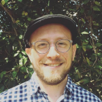 A smiling guy with a beard, classes, and a hat meant to hide male-pattern baldness.