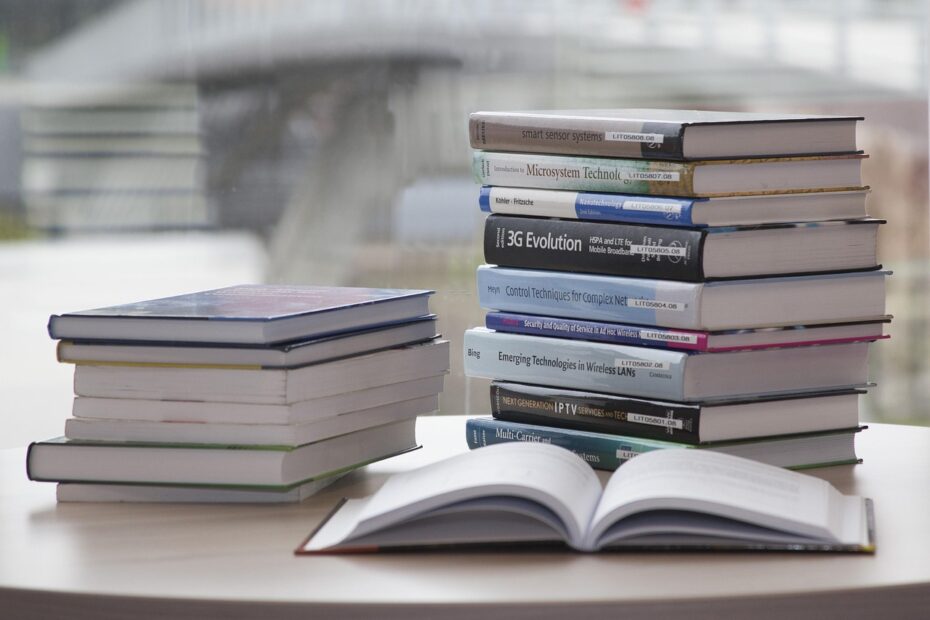 Stacks of hardcover books on a round table, with one book open in the foreground and a blurred background.