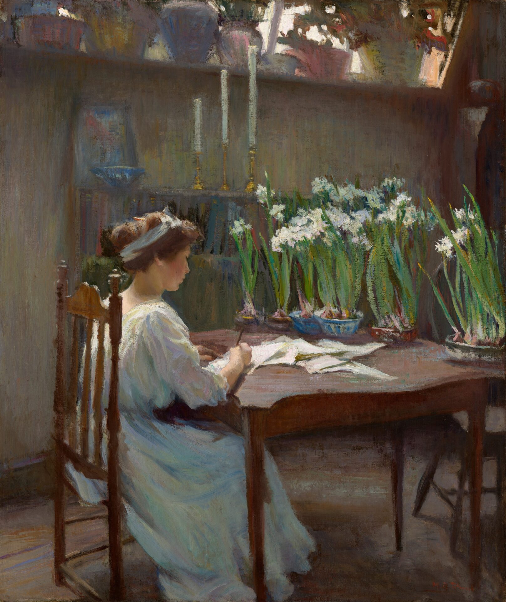 This painting shows a woman in profile, sitting at a wooden table strewn with papers, her body angled away from us. She has pale skin and rosy cheeks, and her light brown hair is tied up and adorned with a light blue headband. She wears a light colored gown that appears mostly white, but also has streaks of light pink, yellow, pale green, and light blue. She is writing on one of the sheets of paper that is scattered on the table. Six potted plants with long green stems and white flowers line the edge of the table across from her. She sits in a room with a brownish-gray wooden floor and pale green walls. There is a bookshelf to the left of the woman, with a framed photograph, a small bowl, and three long white candlesticks of varying heights on top of it. Above the bookshelf is a tall window ledge which is also lined with leafy plants in pink, yellow, light blue, and white pots. White light shines in from between the plants, casting a bright glow on the back of the woman and faint shadows below the table and the chair she sits on. The brushstrokes of the painting, especially those in the background, are visible, giving the painting a slightly hazy quality.
