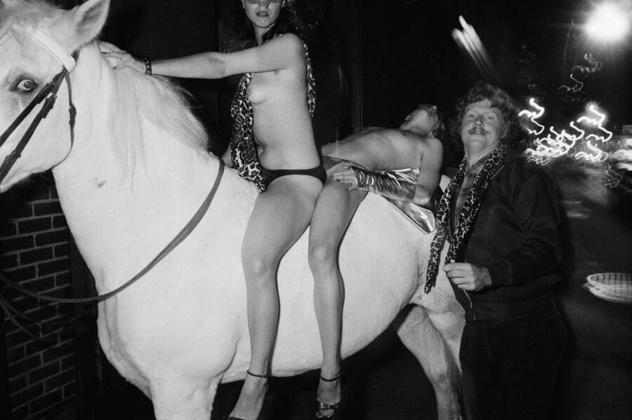 A woman and a man laying on his back ride a horse through Studio 54.