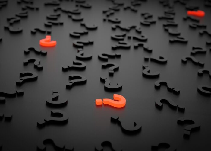 A computer-rendered pile of black question marks on a black background is punctuated by three scattered orange question marks that glow.