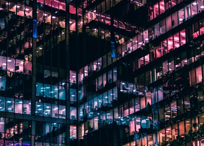The glass windows of two intersecting wings of an office building are lit up at night.