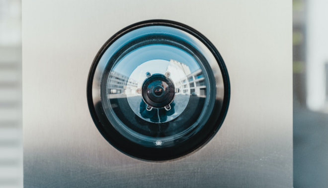 A faceless figure taking a picture is reflected in the convex lens of the camera they're photographing.