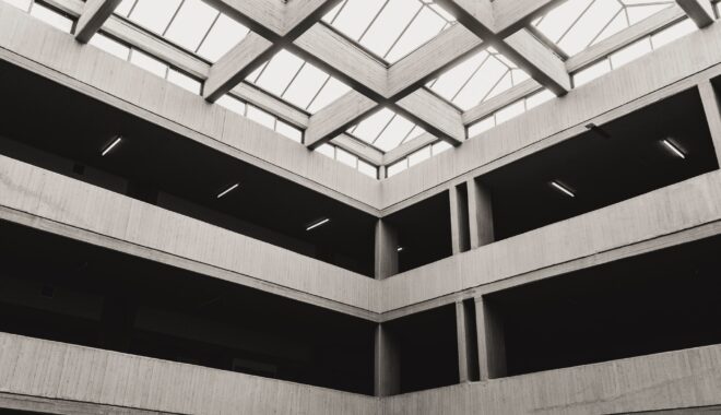 Grey, black and white corner of a multi-story building with light streaming through the ceiling.