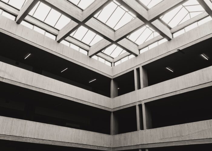 Grey, black and white corner of a multi-story building with light streaming through the ceiling.
