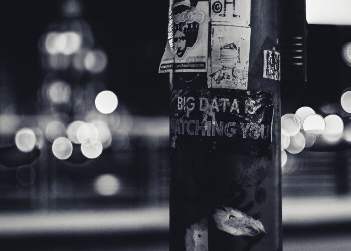 A telephone poll in black and white at night has a poster on it that reads 'Big Data is Watching You.'
