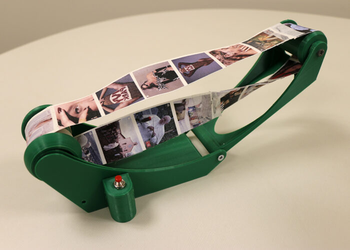 Final 3D-printed version of the Möbius Machine. Green plastic allows a canvas strip of instagram feeds to pass through in an infinite loop on a spindle.