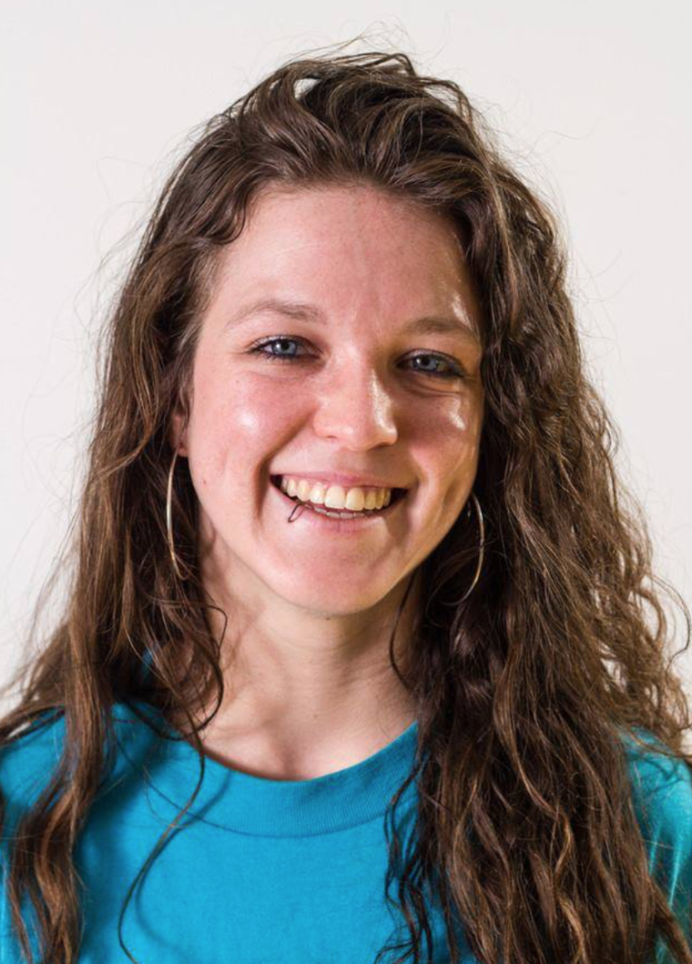 Jenna Queenan headshot with white background, smiling wearing a blue shirt