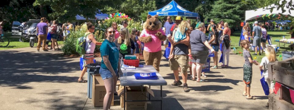 Woman standing at admissions table at the entry of a busy event. A squirrel mascot is nearby.