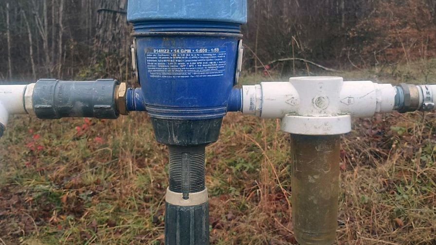 A Dosatron fertilizer injector installed in an open field for crop and plant applications.